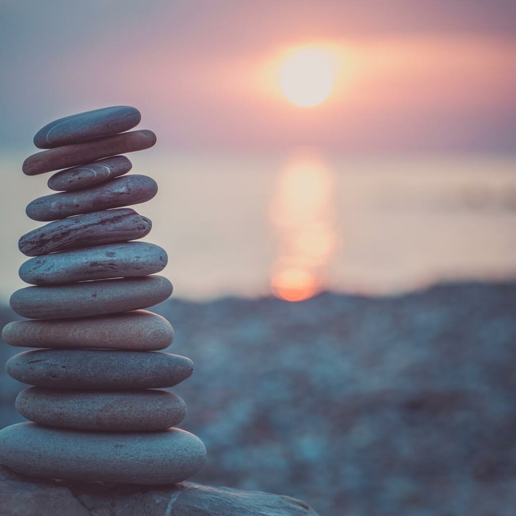 stones pyramid on sand symbolizing zen, harmony, balance. ocean at sunset in the background
