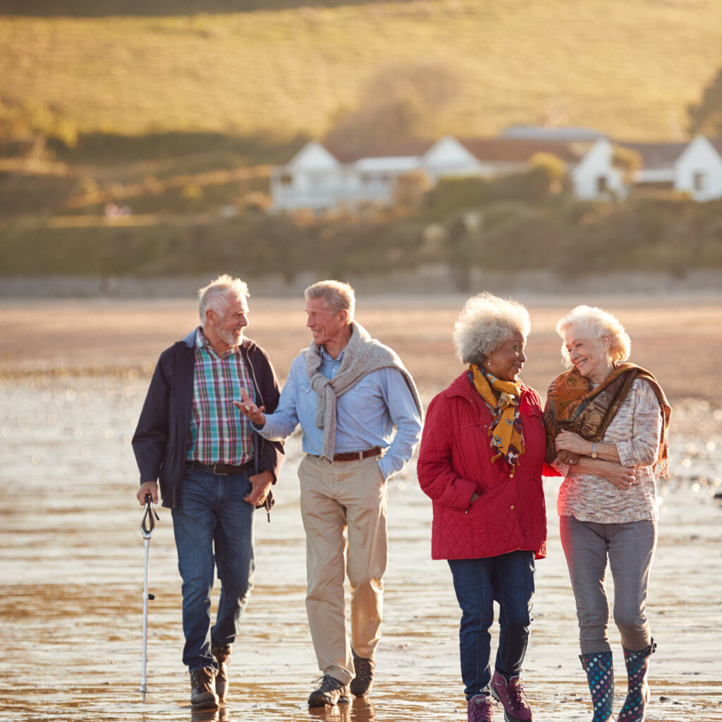 group of smiling senior friends walking arm in arm along shoreline of winter beach