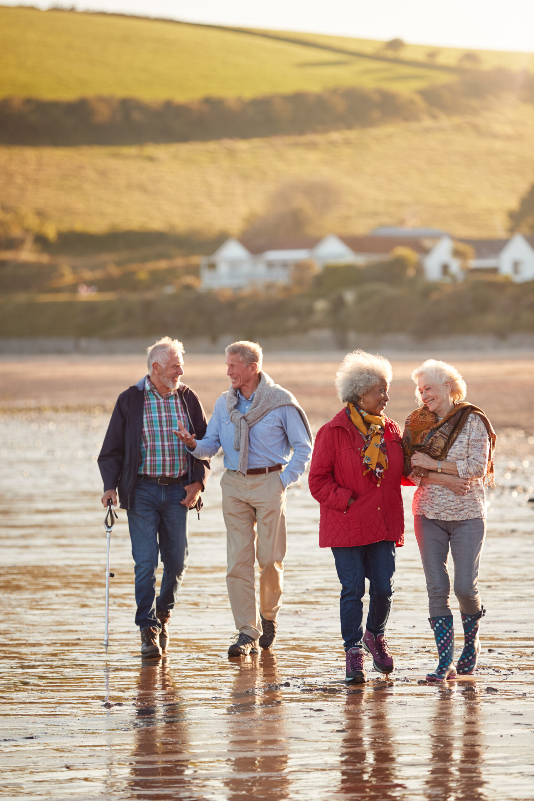 group of smiling senior friends walking arm in arm along shoreline of winter beach