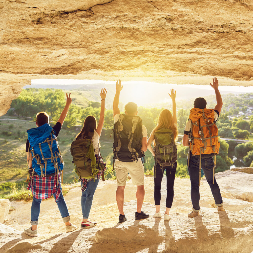 group of travelers with backpacks standing at the cave entrance and admiring the view